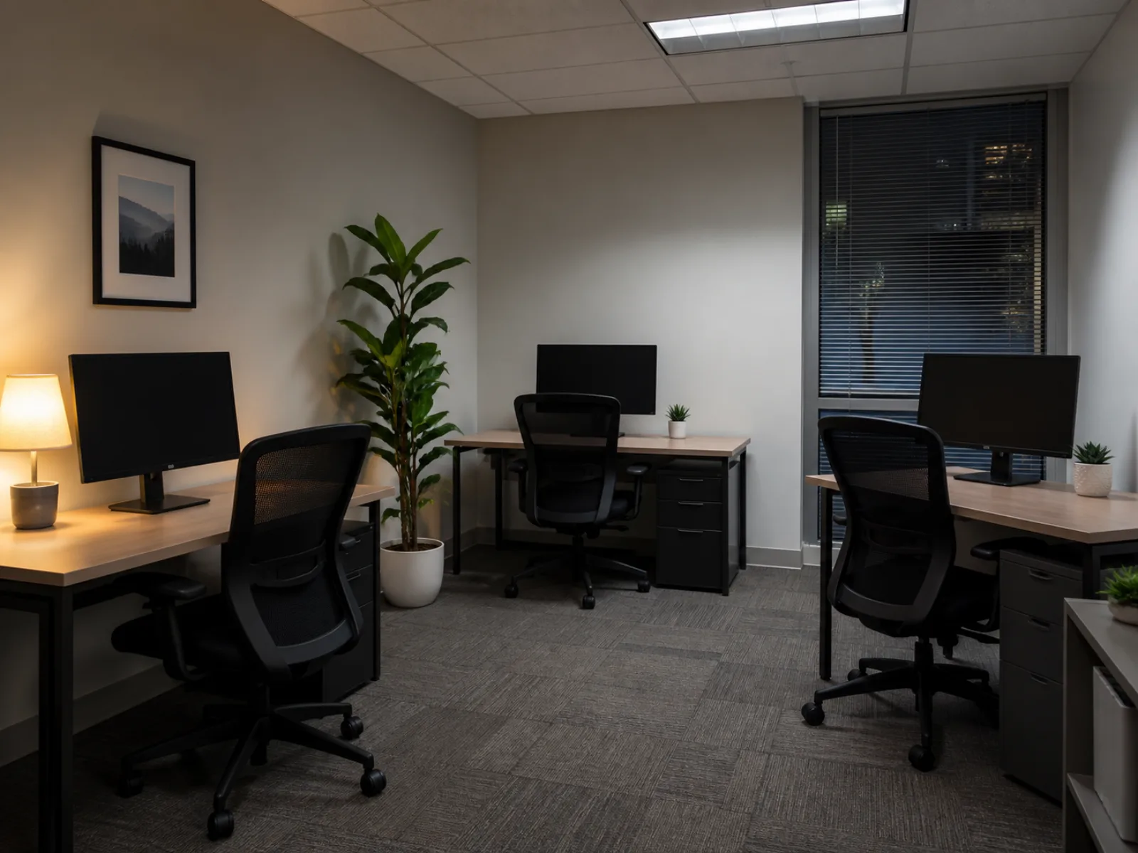 Small office with three empty desks and dark monitors after hours